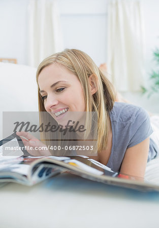 Happy casual young woman reading magazine while lying on couch at home