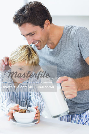 Smiling father pouring milk for sons cereal at breakfast