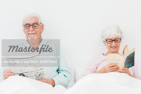 Happy elderly couple reading in bed