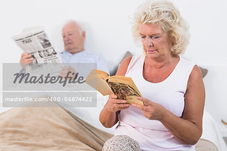 Aged couple reading a book and newspaper on the bed