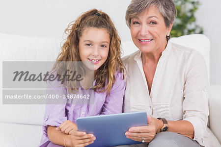 Little girl and her grandmother looking at the camera with tablet pc in sitting room