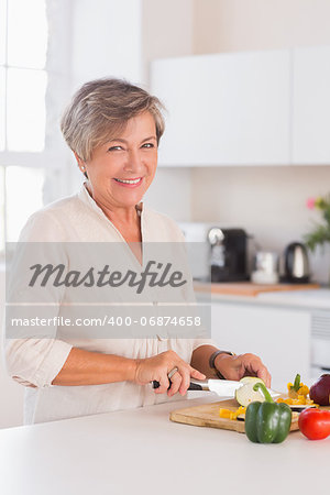 Old woman cutting vegetables on a cutting board with a smile in kitchen