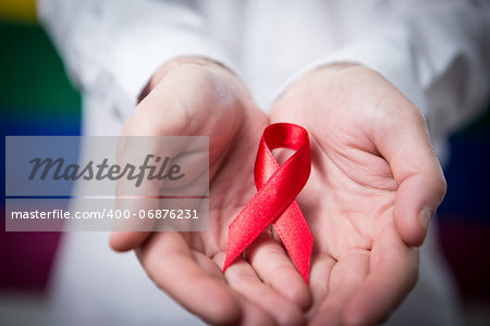 Man in shirt holding red aids ribbon on rainbow background