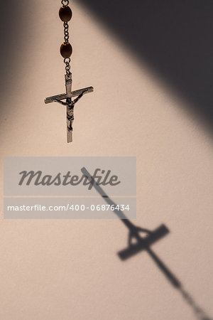 Crucifix from rosary beads hanging and casting a shadow