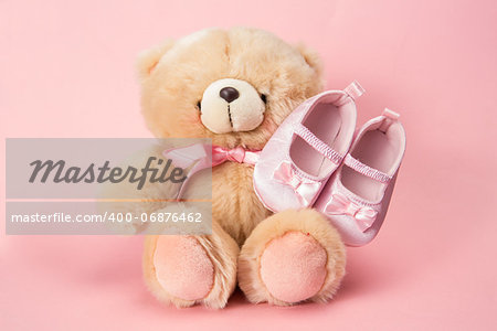 Fluffy teddy with pink ribbon and baby booties on pink background