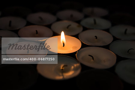 Single candle lighting surrounded by others in the darkness