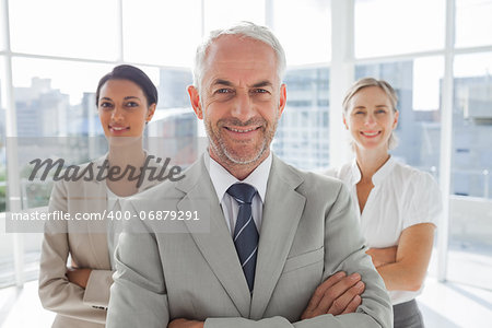 Smiling businessman standing in front of colleagues with arms folded