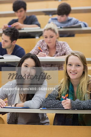 Smiling students sitting in a lecture hall while taking notes