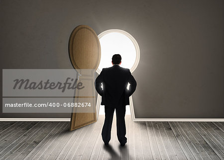 Buisnessman looking at keyhole shape door revealing light in dark grey room
