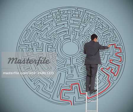 Businessman on ladder drawing red line to solve a maze on grey wall
