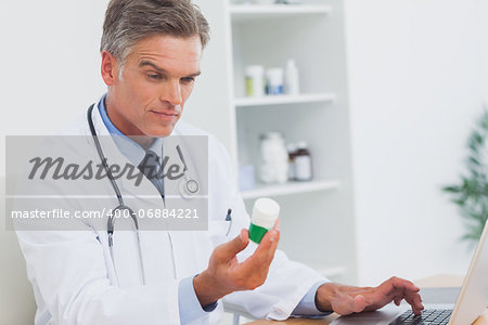 Serious doctor holding a bottle of pills and his using laptop
