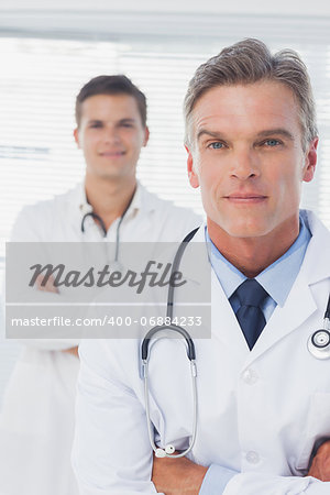 Serious doctor with arms crossed standing in front of his colleague