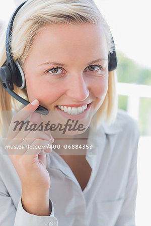 Businesswoman touching headset and smiling at camera in her office