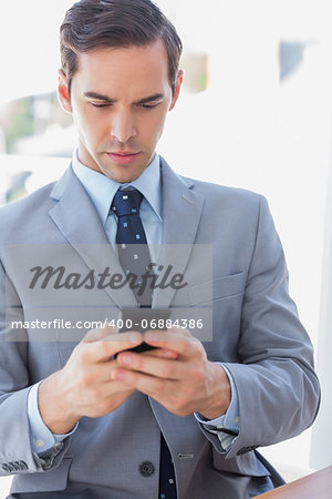 Serious businessman texting on phone in his office
