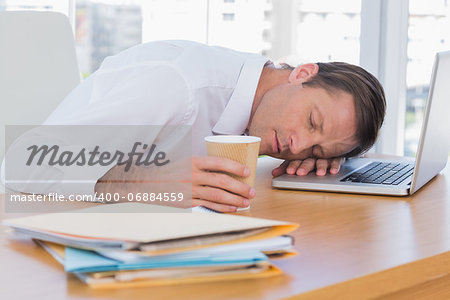 Businessman sleeping on a laptop while he is holding a cup of coffee