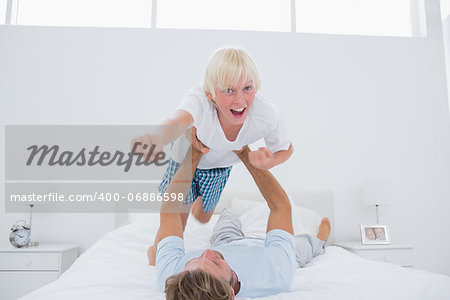 Father playing airplane holding his son in bed