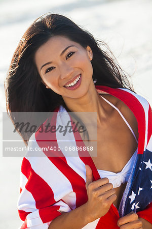 Beautiful young Chinese Asian woman laughing wearing bikini and wrapped in American flag towel on a sunny beach