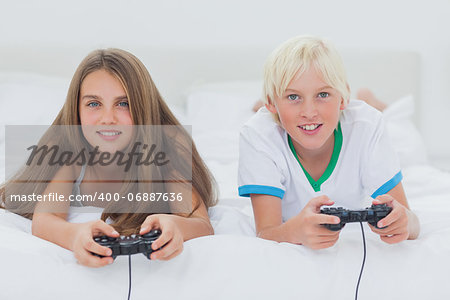 Portrait of siblings playing video games while they are lying on bed