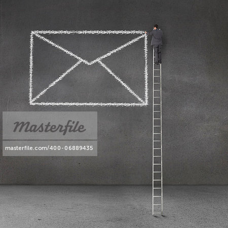 Businessman drawing a giant envelope on a grey wall and standing on a giant ladder