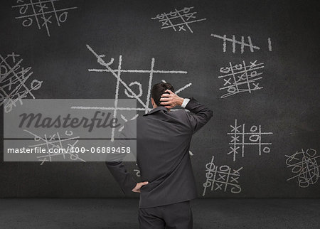 Thoughtful businessman looking at Tic-tac-toe game drawn on a chalkboard