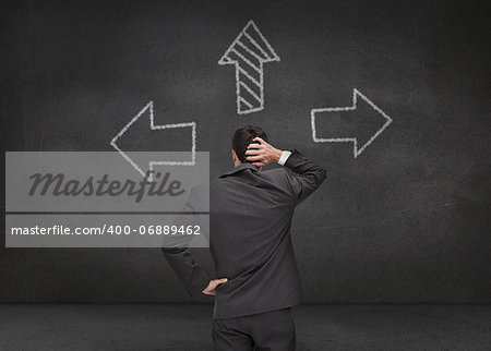 Thoughtful businessman looking at three arrows drawn on chalkboard