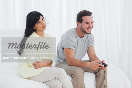 Annoyed woman looking up during her boyfriend laughing and playing video games