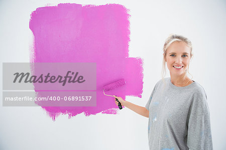 Happy young woman painting her wall pink and smiling at camera