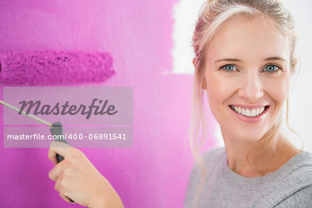 Smiling woman painting her wall in pink and looking at camera