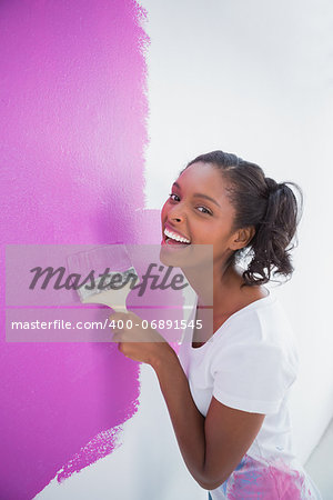 Laughing young woman painting her wall in pink and smiling at camera