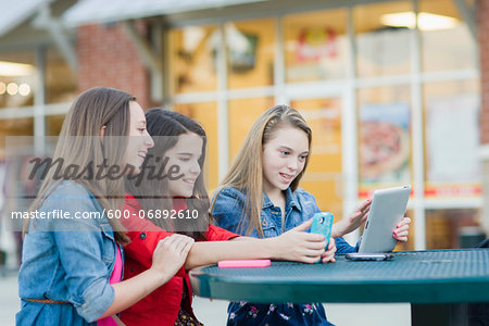 Girls using Cell Phone and Tablet Computer at Outdoor Cafe, USA