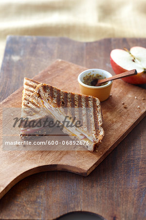 Grilled Cheese Panini with Cheddar and Apple Cut in Half on Cutting Board with half a Red Apple and Dijon Mustard in small Bowl, Studio Shot