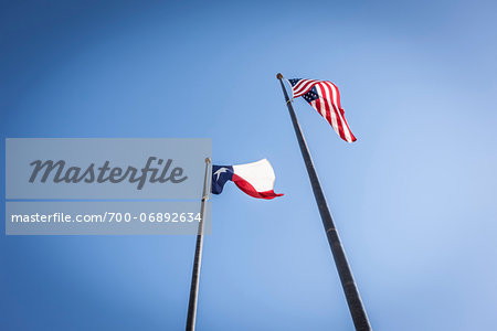 Low Angle View of Texas and US Flags Against Blue Sky Low Angle View of Texas and US Flags Against Blue Sky
