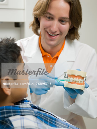 Dentist showing young boy how to brush teeth on model