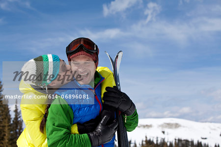 Young woman in skiwear kissing mature man holding skis