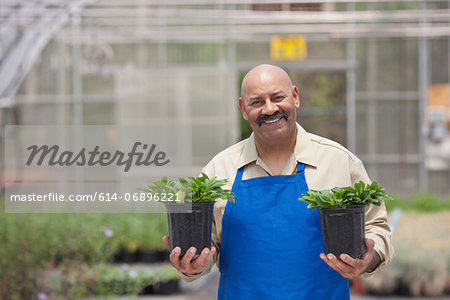 Mature man holding plant pots in garden centre, portrait