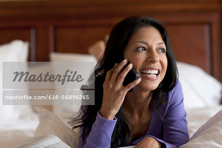 Mature woman lying on bed using mobile phone, smiling