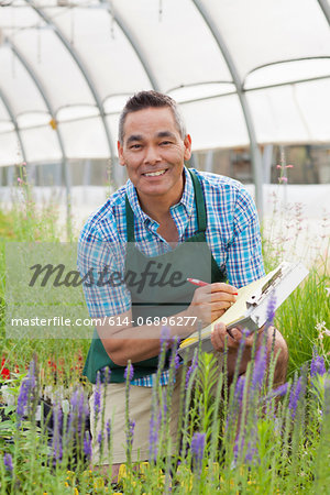 Mature man holding clipboard in garden centre, portrait