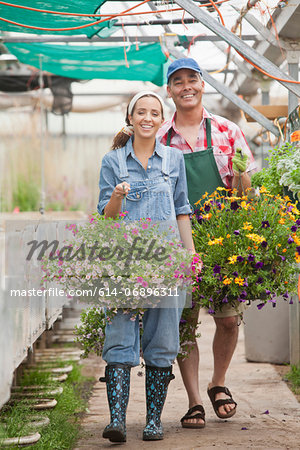 Young woman and mature man walking with hanging baskets in garden centre