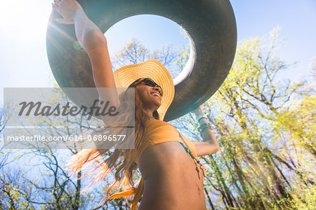 Woman wearing hat and sunglasses carrying inner tube above head