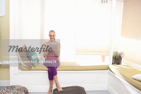 Woman sitting on window seat drinking using digital tablet