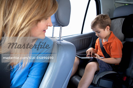 Mother watching son use digital tablet in back seat of car