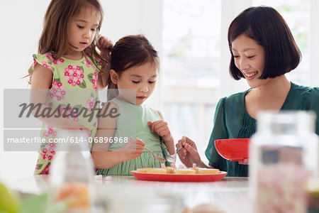 Mother and two daughters spooning topping onto tarts