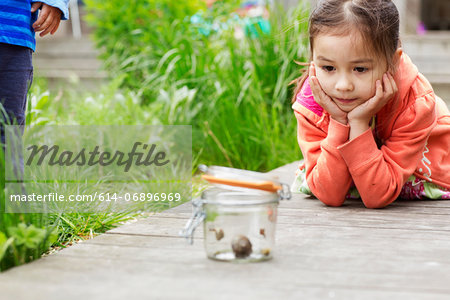 Young girl in garden watching jar of snails Young girl in garden watching jar of snails