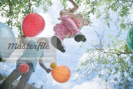 Young girls jumping on garden trampoline with balloons