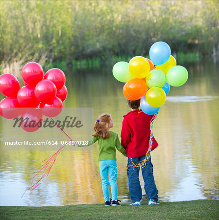 Brother and sister holding balloons in park