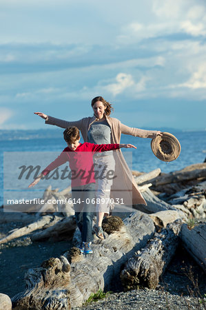 Mother and son walking along tree trunk at coast