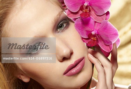 Close up portrait of young woman holding orchid stem
