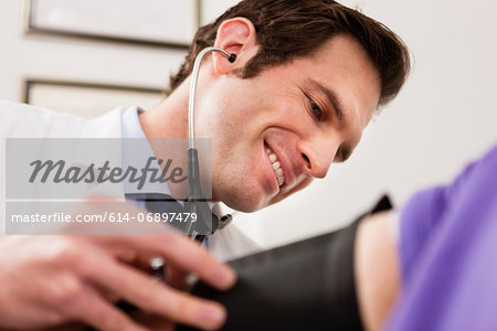 Mid adult doctor using stethoscope and blood pressure cuff on patient, close up