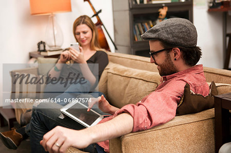 Couple sitting on sofa using digital tablet and smartphone