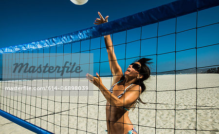 Female beach volleyball player hitting ball over net